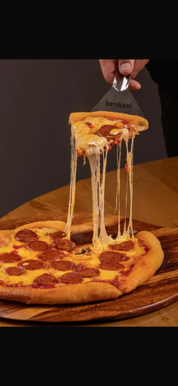 Pizza de pepperoni BIGA sobre una tabla de madera, con una porción en la mano